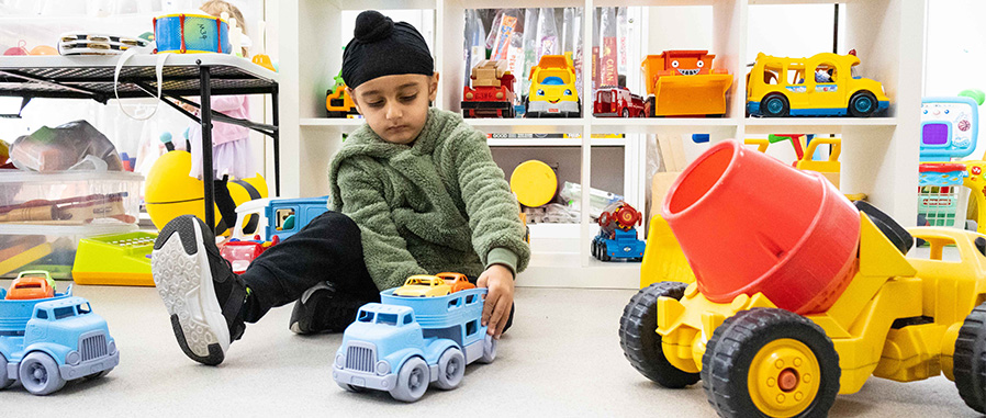 child playing with a toy truck with several other assorted toys around them in a toy library