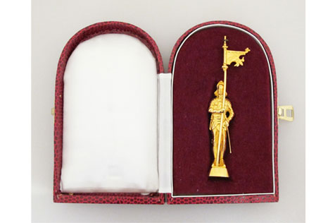 Gold figure holding a flag in a maroon presentation box