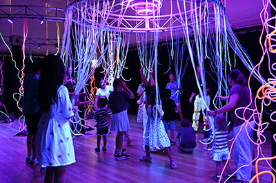 Kids on stage with illuminated ribbons suspended from ceiling