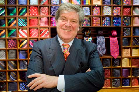 Smiling man in a suit tanding in front of a shelves displaying brightly coloured neckties.