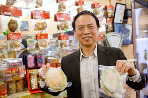 Man holding two large shells in plastic bags in front of a display of packaged goods.