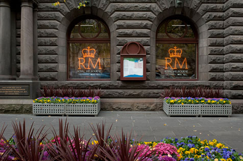 Exterior view of the Melbourne Town Hall, A crown and the letters RM painted in bright orange on each of two arched windows