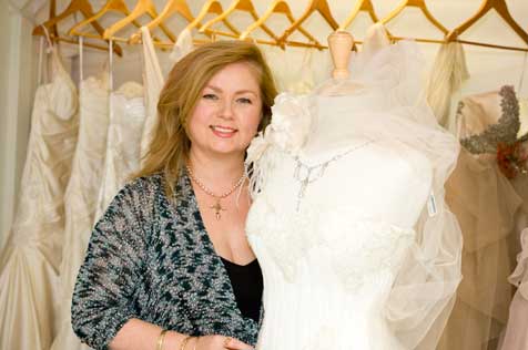 Woman holding a white wedding dress standing in front of a rack of wedding dresses.