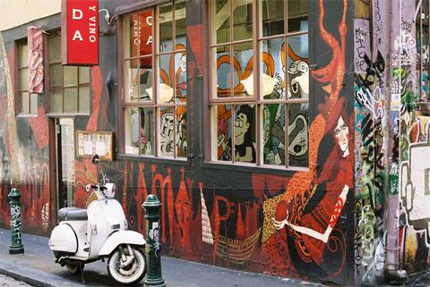 External wall of Movida painted with red and black street art, with a moped parked outside.