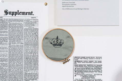 Close-up of an embroidery hoop featuring a stitched crown next to a newspaper article headed 'Supplement'