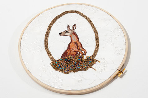 Embroidery hoop featuring a brown kangaroo pearing out of a loop of gold stitching