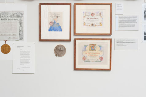 Wall with three framed certificates, large medal, embroidery hoop and  other ephemera