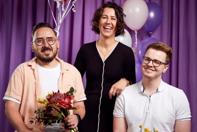 Three people holding flowers and balloons in front of a curtain
