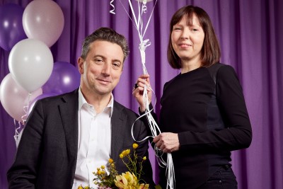 Two people with flowers and baloons in front of a purple curtain