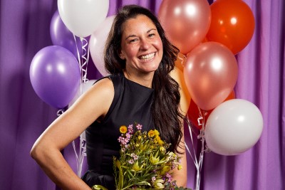 A person holding flowers next to balloons in front of a purple curtain