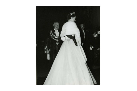 Black and white photo showing the back of Queen Elizabeth, wearing a white fur