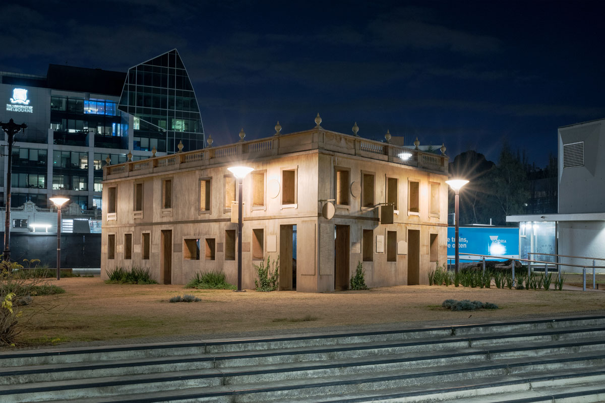 Photograph of art installation made to look like wooden building facade at night in the city.