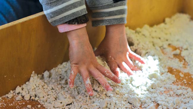 A child's hands playing with a crumbly dough-like substance