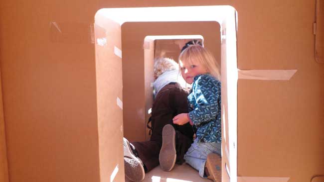 Two children clambering through a corridor made from cardboard boxes