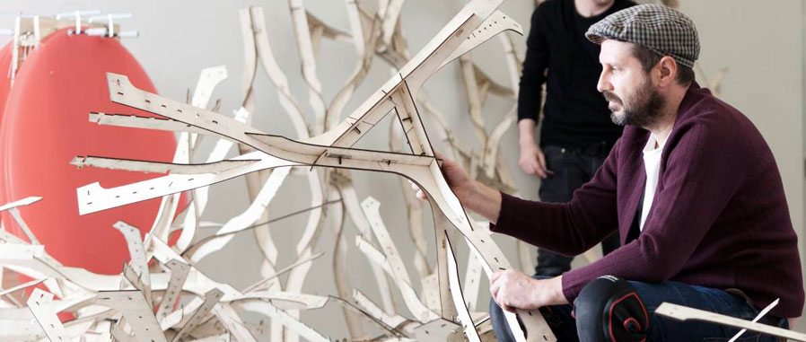 An artist assembling an intricate sculpture of interlocking branch-like parts