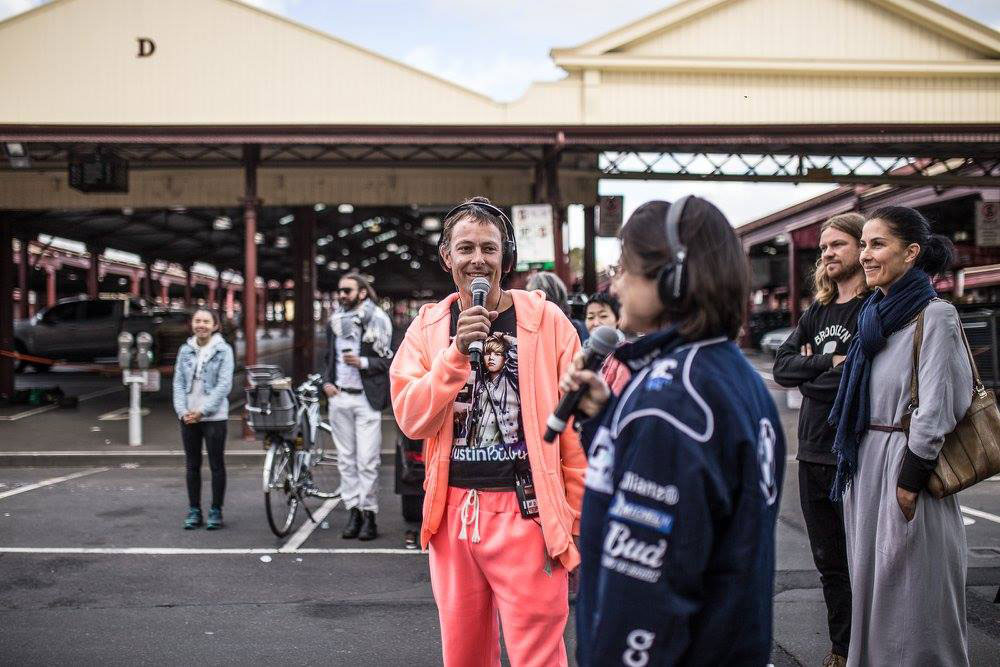 A man and a woman with microphones talking to a crowd at the Queen Victoria Market