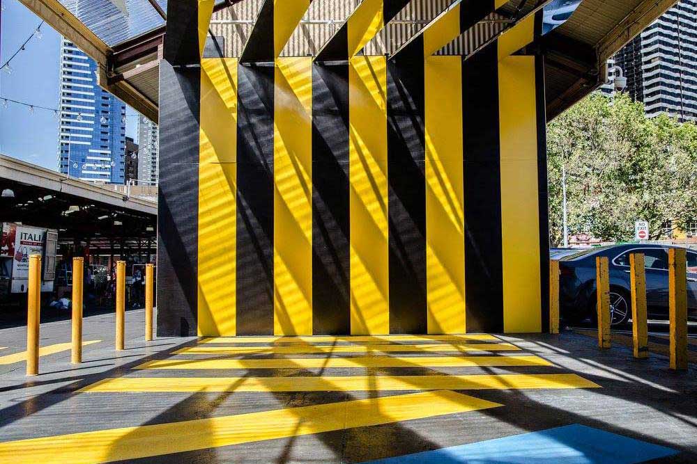 An artwork at the Queen Victoria Market - black and yellow stripes on the ground and going up a wall, with mirrors on the roof. The strips are arranged to sit at the same angles as the Hoddle Grid.