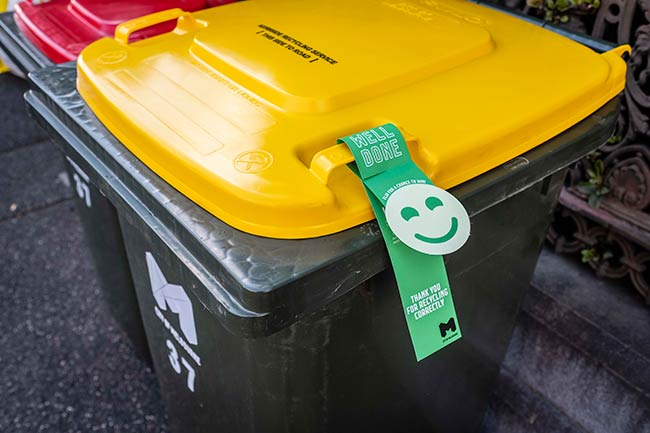 Green bin tag attached to a recycling bin. The tag says 'Well done. Thank you for recycling correctly' and has a smiley face.