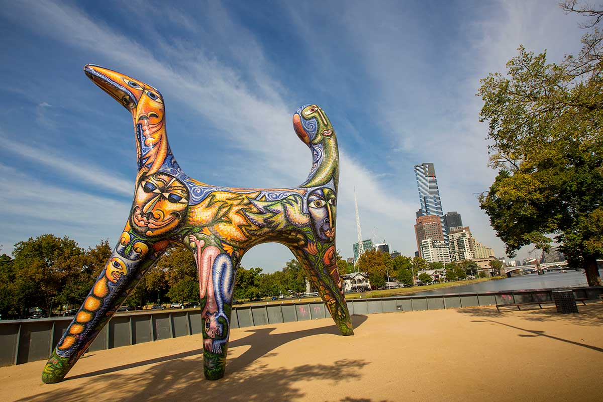 Large sculpture of whimiscal creature with three legs, covered in bright, hand-painted ceramic tiles.