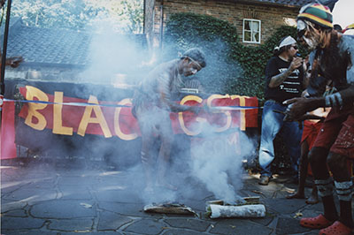 Aboriginal people performing smoking ceremony with banner and building in background