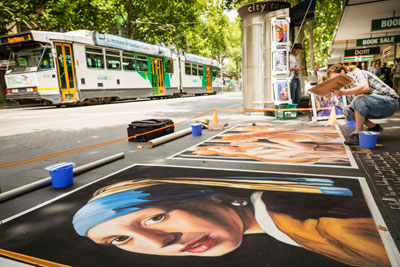 A busker drawing large images on the pavement, including a reproduction of 'Girl with a pearl earring'