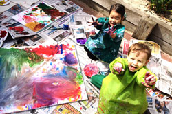 Children painting and holding up their paint covered hands to the camera.