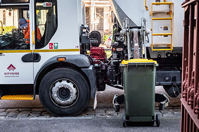 A waste collection truck about to empty a recycling bin.