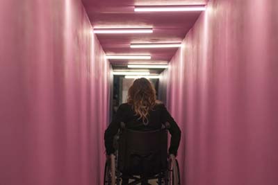 Person in a wheelchair moving through a narrow pink-painted hallway