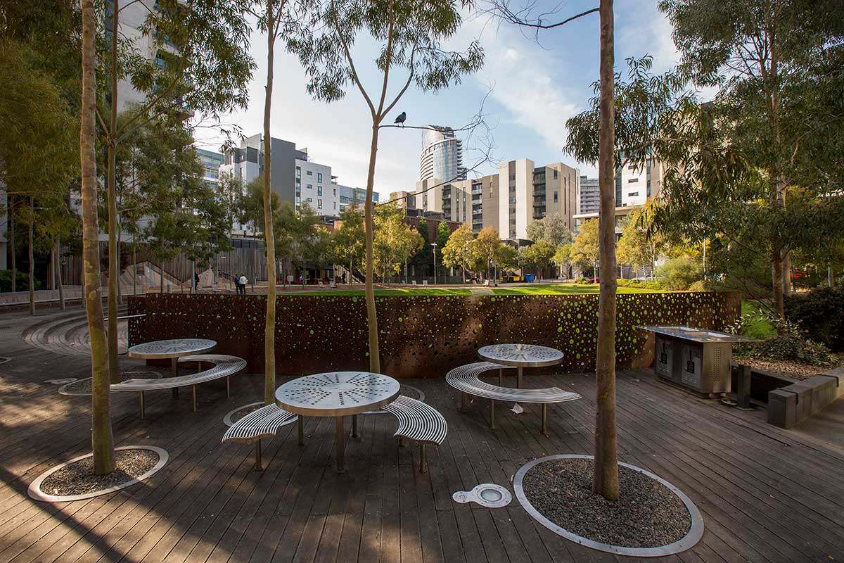 Round metal tables with seating on decked area of Docklands Park.