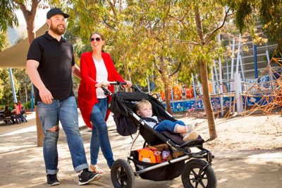 A couple with a child in a pram, walking in a park
