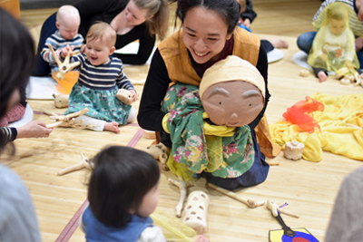 A woman holds a puppet infront of a group of children