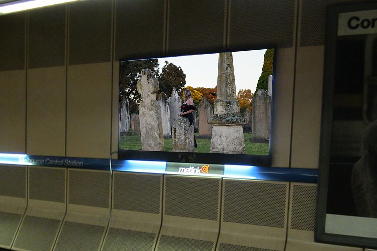 Wall of railway tunnel with video screen showing young woman in a graveyard