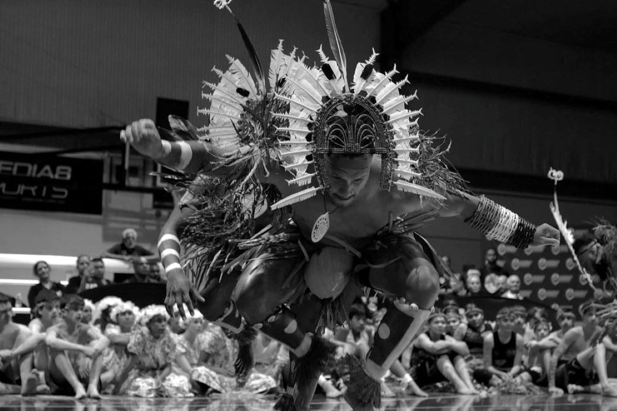 Dancers from the Gerib Sik Torres Strait Islander Dance Troupe. This Troupe is performing at the 2023 Mabo Day Concert. Black and white image of two male dancers in traditional dress performing a dance move in front of a crowd.