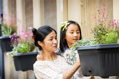 A parent and child looking at a mounted planter box with flowers in it. 