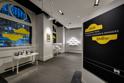 Entrance to the exhibition featuring large black and yellow sign and small tables in front of a large mirror