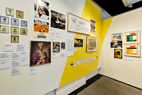 Corner of a wall covered with photos, paintings and images including a picture of a king and a hand-written sign saying 'We want justice'