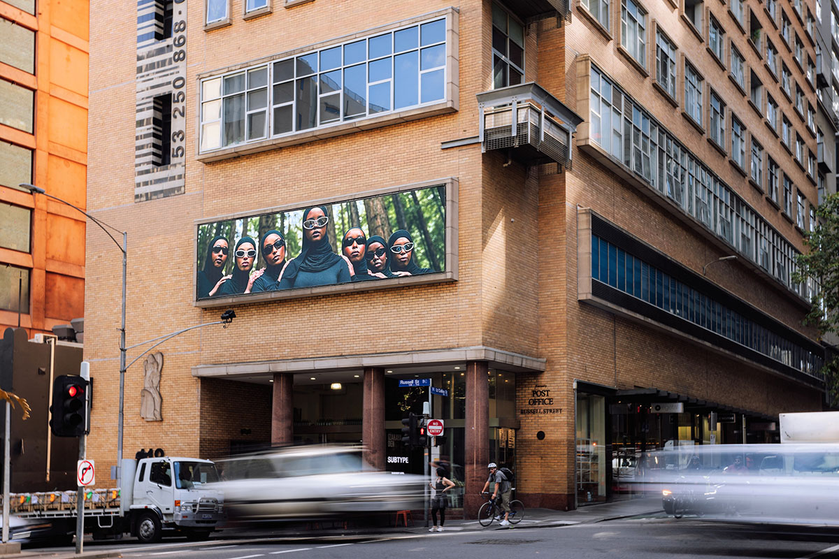 A large billboard image on an orange-brick building depicting a group of women wearing hijabs and sunglasses.