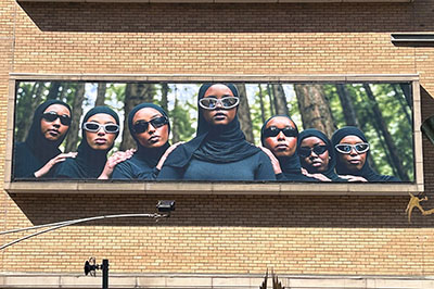 A large billboard on an orange-brick building depicting women in muslim headgear and dark glasses