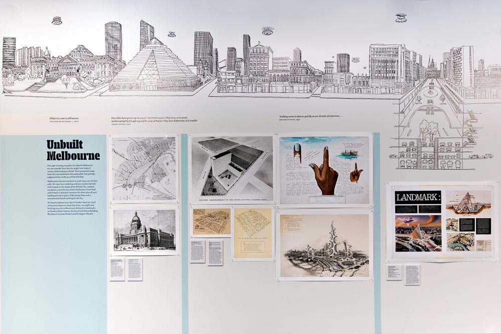 'Unbuilt Melbourne' exhibits showing maps/plans of unusual landmarks including a glass pyramid and hand with finger pointing upwards. A section of the mural is shown above which includes scenes with flying vehicles layers of streets underground
