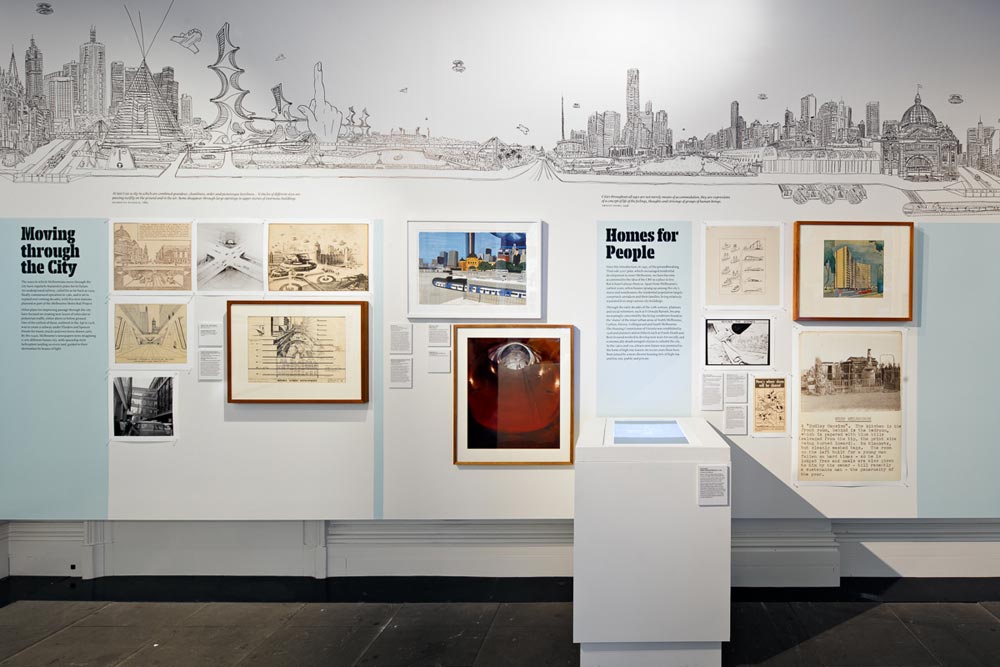 View of exhibits titled 'Moving through the City' and 'Homes for People' beneath section of mural showing buildings of existing and futuristic Melbourne cityscape