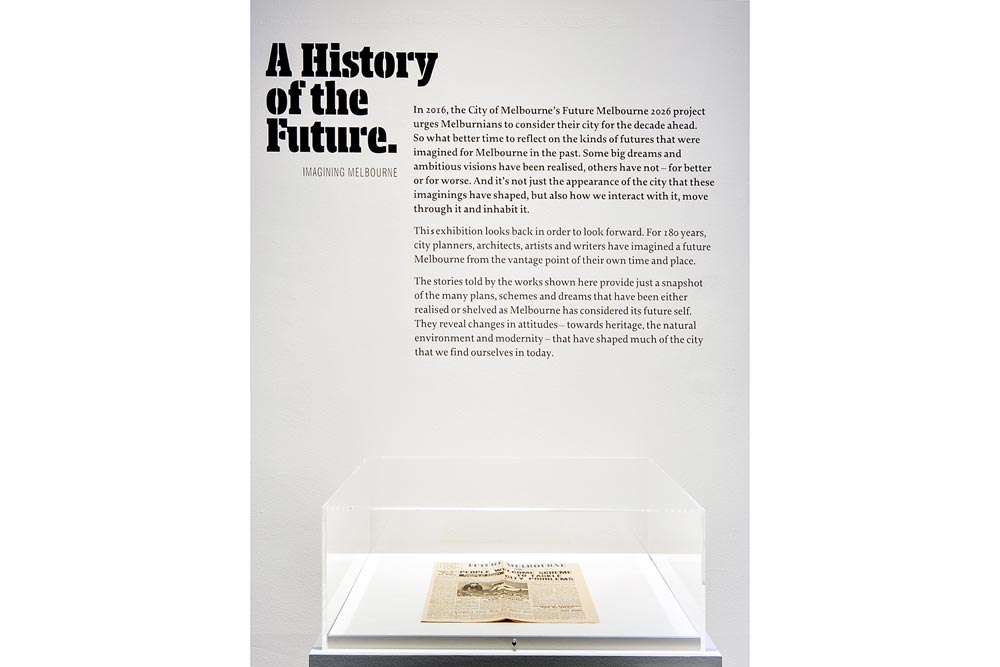 'A History of the Future' sign giving an introduction to the exhibition. Below the sign is a newspaper exhibited in a glass cabinet.