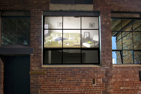 Red brick building facade with image of a loungeroom projected on its window