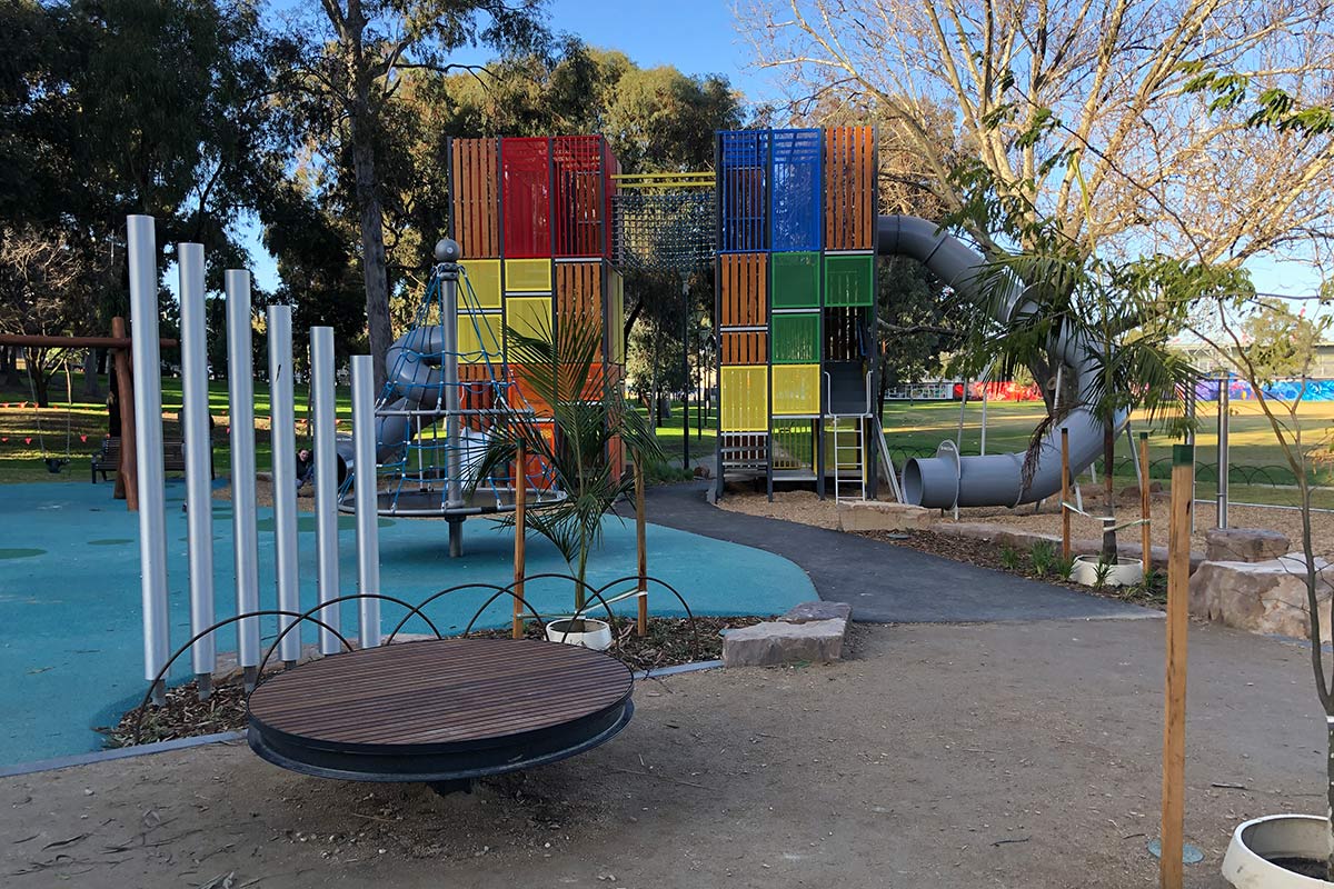 Playground with various equipment including two tall towers clad in coloured panels, a conical rope dome and tube slides.