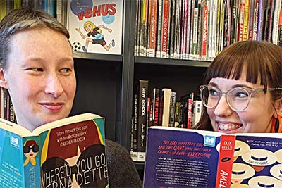 Two people reading books in front of library shelves.