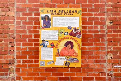 Poster with illustration of 'Lisa Bellear: Warrior Woman' and accompanying text, attached to brick wall