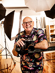 Andrew Campbell holding a camera in his studio, with light-reflecting panels in the background.