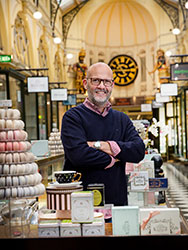 Andrew White standing in The Little Royal kiosk in Royal Arcade, surrounded by gift boxes and a display of macarons.