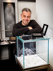 Frank Athanasopoulos in his showroom, leaning on a glass display cabinet containing jewellery.
