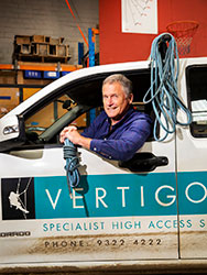 John Dollisson leaning out of a Vertigo company vehicle holding a bundle of rope. 