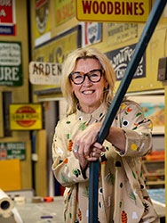 Kim Lewis in the workshop surrounded by various business, street and vintage signs.